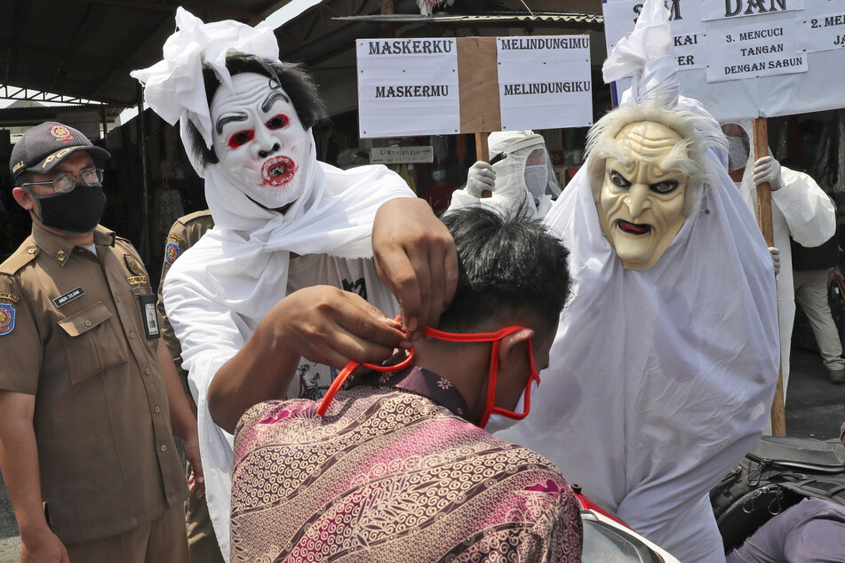 Mitarbeiter der indonesischen Gesundheitsbehörden, verkleidet als "Pocong"-Geister, klären Passanten über die Corona-Maskenpflicht und Abstandsregeln auf.