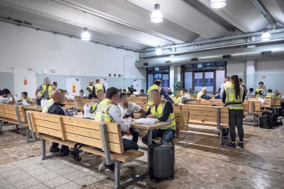 Polizisten warten mit Ausreisepflichtigen auf dem Flughafen Leipzig in einer Abflughalle. Tische und Bänke wurden besonders massiv ausgeführt, um mögliches Randalieren zu vermeiden.