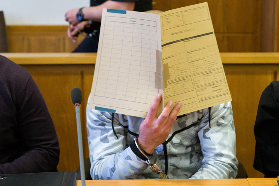 Der im Mordprozess angeklagte 22-Jährige Syrer verdeckte in einem Saal des Landgerichts Oldenburg (Niedersachsen) sein Gesicht mit einem Aktendeckel.