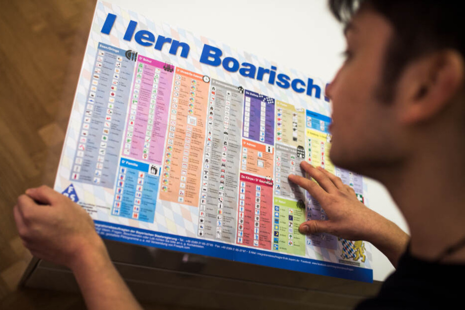 Ein Mann liest die Sprachtafel "I lern Boarisch". In München geht de Streit um das Integrationsgesetz weiter. (Symbolbild))