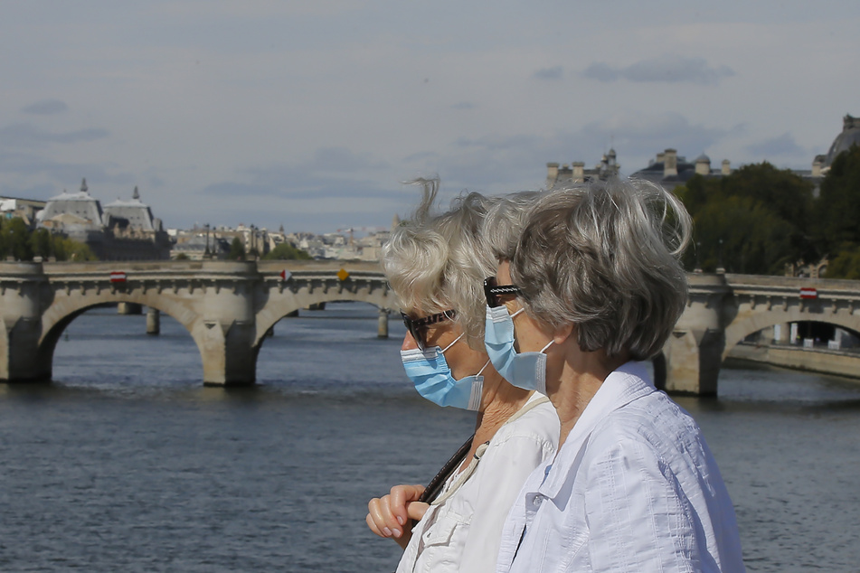 Paris: Zwei Passantinnen mit medizinischem Mundschutz spazieren über eine Brücke.