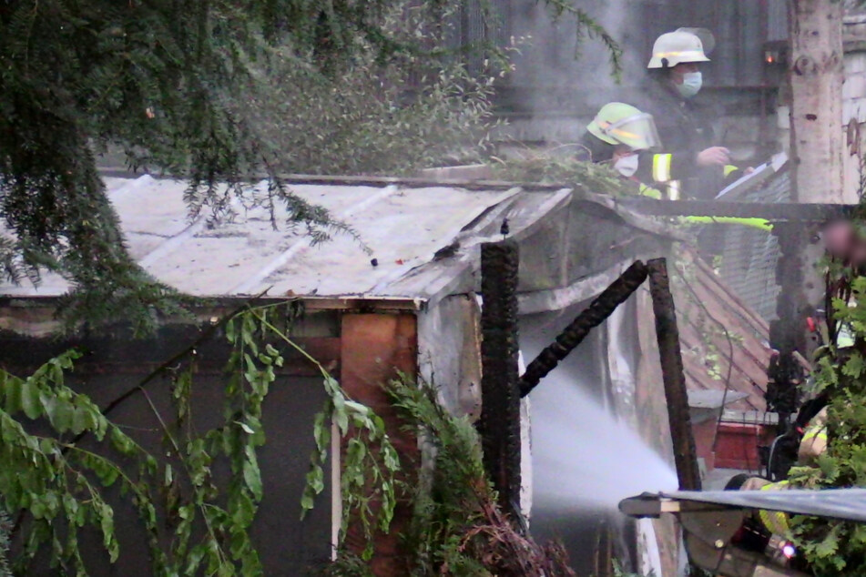 Gartenlaube geht in Flammen auf: Feuerwehr muss zur Kettensäge greifen