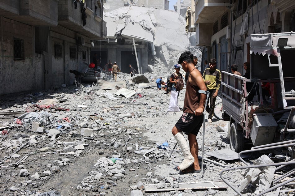 An injured youth walks on debris as Palestinians salvage items from the rubble of homes destroyed in Israeli strikes on the southern al-Zeitoun neighborhood in Gaza City on August 19, 2025.