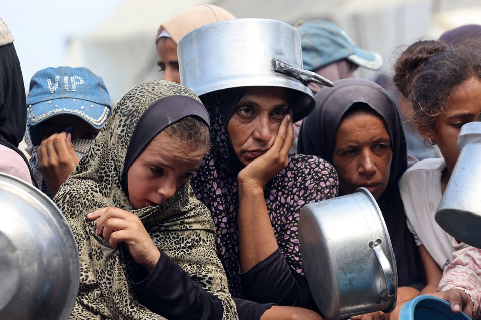 Palestinian women and children wait to receive food from a charity kitchen, in Khan Younis in the southern Gaza Strip on August 21, 2025.
