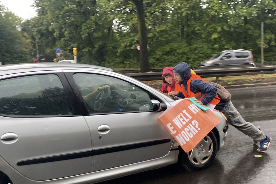 Ein Auto schiebt Klimaschützer bei einer Protestaktion in München vor sich her.