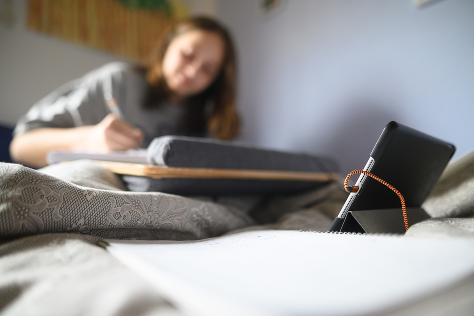Eine Schülerin arbeitet hinter einem Tablet in ihrem Bett für die Schule.