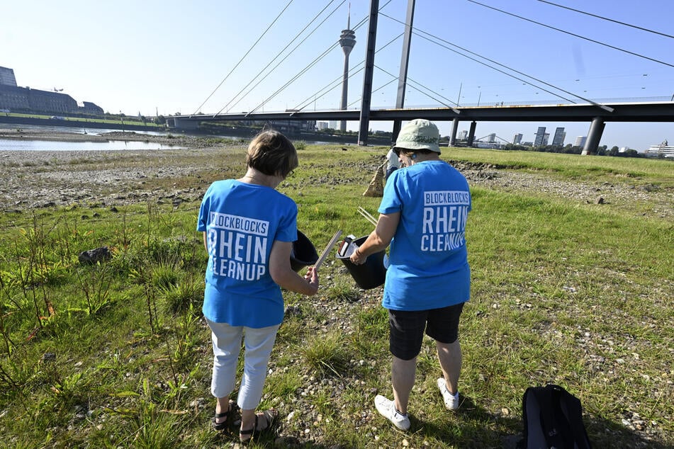 Zwei Freiwillige der Aktion RheinCleanUp helfen beim Einsammeln von Unrat entlang des Rheinufers in Düsseldorf. (Archivbild)