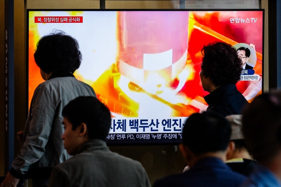 People in Seoul, South Korea, walk past a television showing a news report on North Korea's "Malligyong-1-1" reconnaissance satellite, which exploded minutes after launch due to a suspected engine problem.