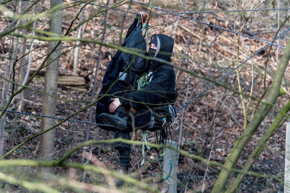 Ein Umweltschützer sitzt auf einem Seil im Bahnhofswald. Polizisten haben mit der Räumung des Waldes begonnen.