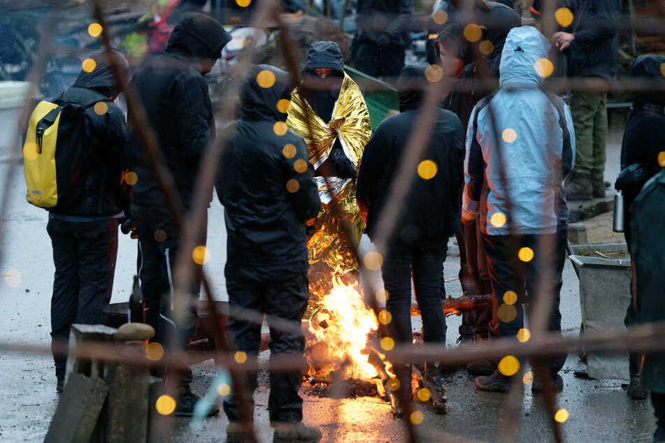 Aktivisten harren bei strömenden Regen am Rand von Lützerath an einem Lagerfeuer aus.