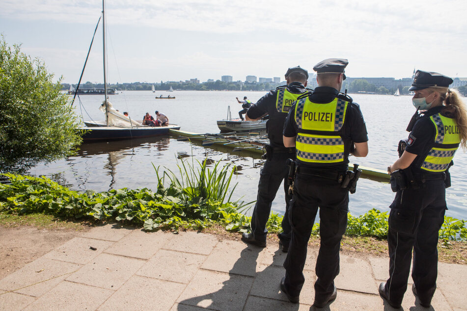 Polizisten stehen an der Alster. Im Hintergrund ist zu sehen, wie das Ruderboot in der Jolle feststeckt.