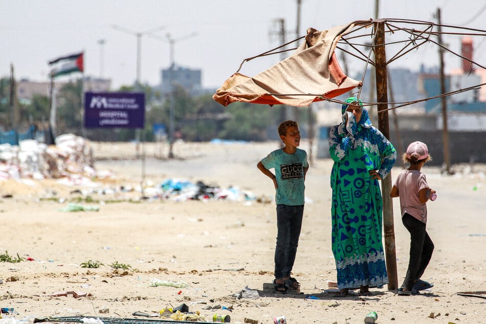 A woman stands with two children under a fraying shade along a street in the western part of Rafah in the southern Gaza Strip on June 14.