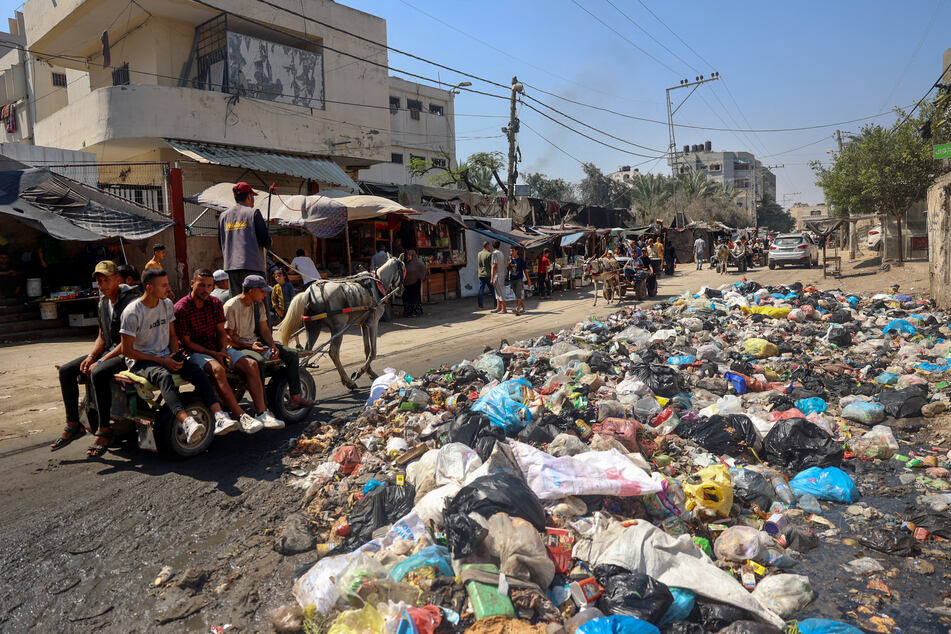 Palestinians ride a donkey-drawn cart past a garbage dump and sewage water on a street in Deir el-Balah in the central Gaza Strip on July 23, 2024, as municipal infrastructures fail due to Israeli bombardment of the besieged Palestinian territory amid the ongoing conflict with Hamas movement.