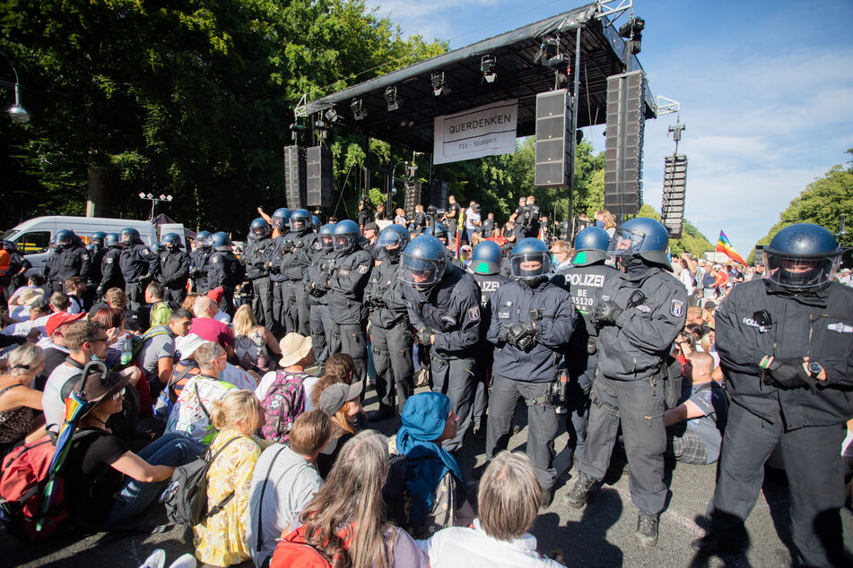 Berliner Polizisten stehen bei einer Kundgebung gegen die Corona-Beschränkungen auf der Straße des 17. Juni zwischen Teilnehmern vor einer Bühne.