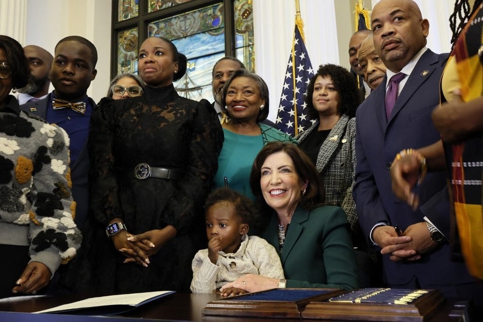 New York Governor Kathy Hochul (c.) smiles after signing legislation to create a state reparations commission on December 19, 2023.