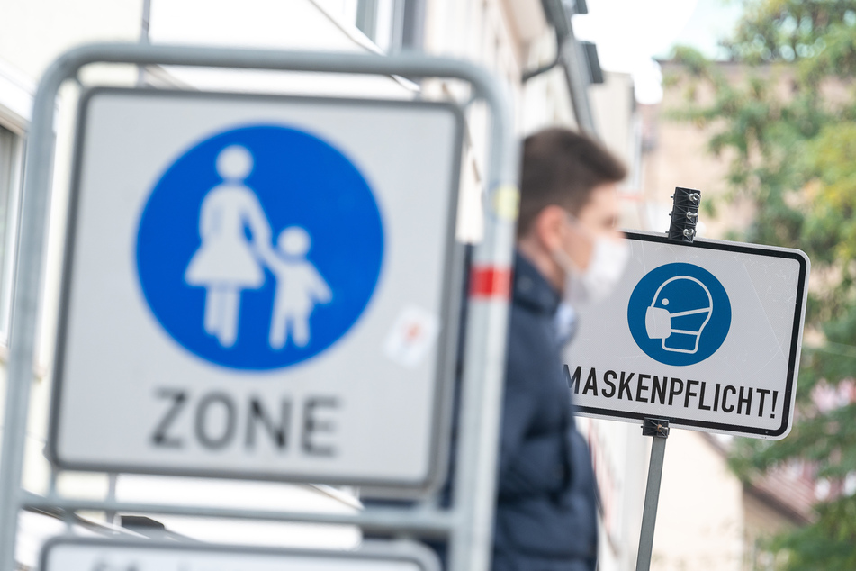 Ein Mann geht in der Fußgängerzone vor einem Schild vorbei, auf dem "Maskenpflicht" steht.