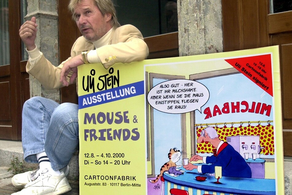 Mit dem Plakat zu seiner Ausstellung zeigt sich der Cartoonist Uli Stein vor der Galerie "Cartoonfabrik" im Jahr 2000 in Berlin.