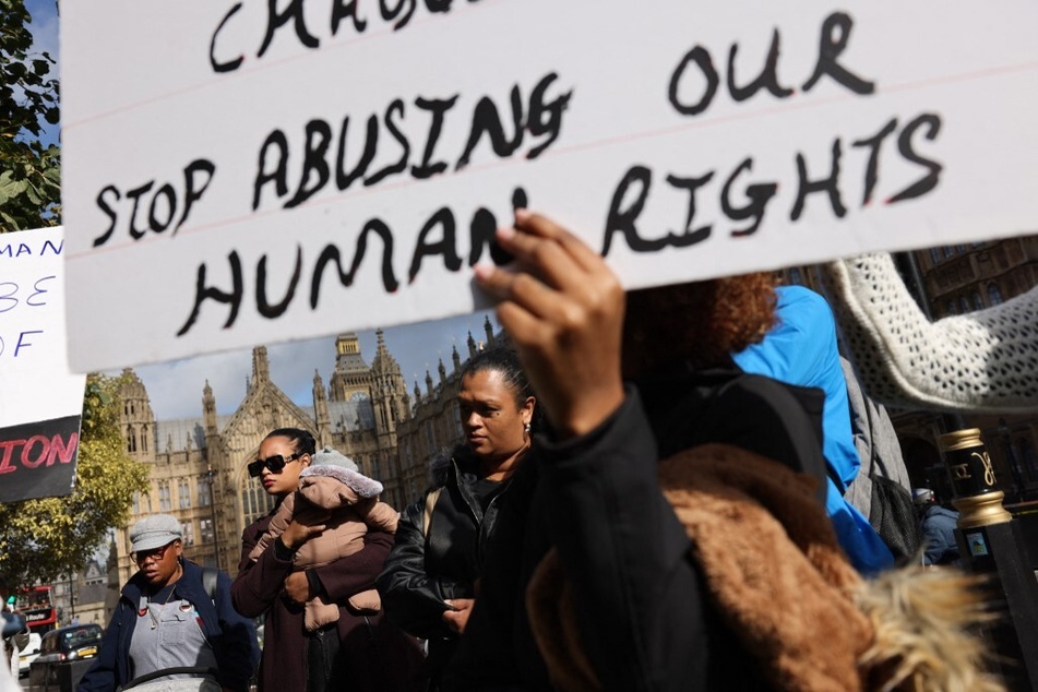 A Chagossian protester outside the UK parliament holds a sign reading "Stop Abusing Our Human Rights."