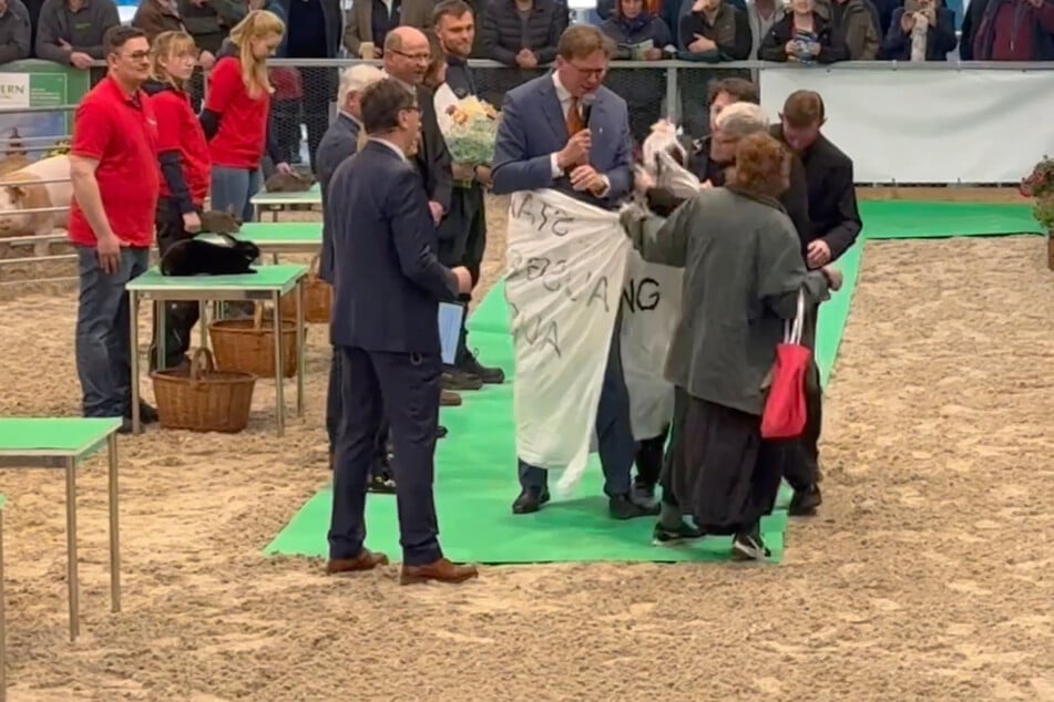 Die Aktivisten stürmten mit einem Banner die Veranstaltung und hüllten kurzzeitig einen Moderator darin ein.