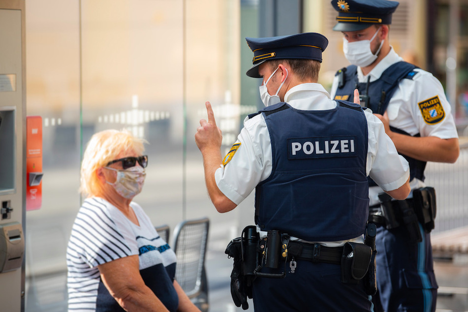 Zwei Polizisten nehmen an einer Tram-Haltestelle in Würzburg von einer Frau nach einem Verstoß gegen die Maskenpflicht die Personalien auf.