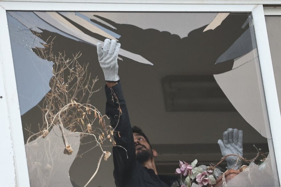 An Israeli policeman collects glass shrapnel from the window of a building that was damaged in an explosion that took place in Tel Aviv on July 19, 2024.