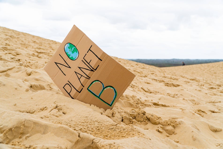 A sign reading "No Planet B" and calling for climate action is pictured in the sand.