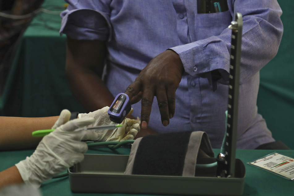 Ein Arzt in Indien überprüft die Vitaldaten eines Mannes, bevor er ihm einen Corona-Impfstoff im Government Fever Hospital verabreicht. Bei der weltweiten Auslieferung der Corona-Impfstoffe kommt es wegen Exportbeschränkungen in Indien zu deutlichen Verzögerungen.
