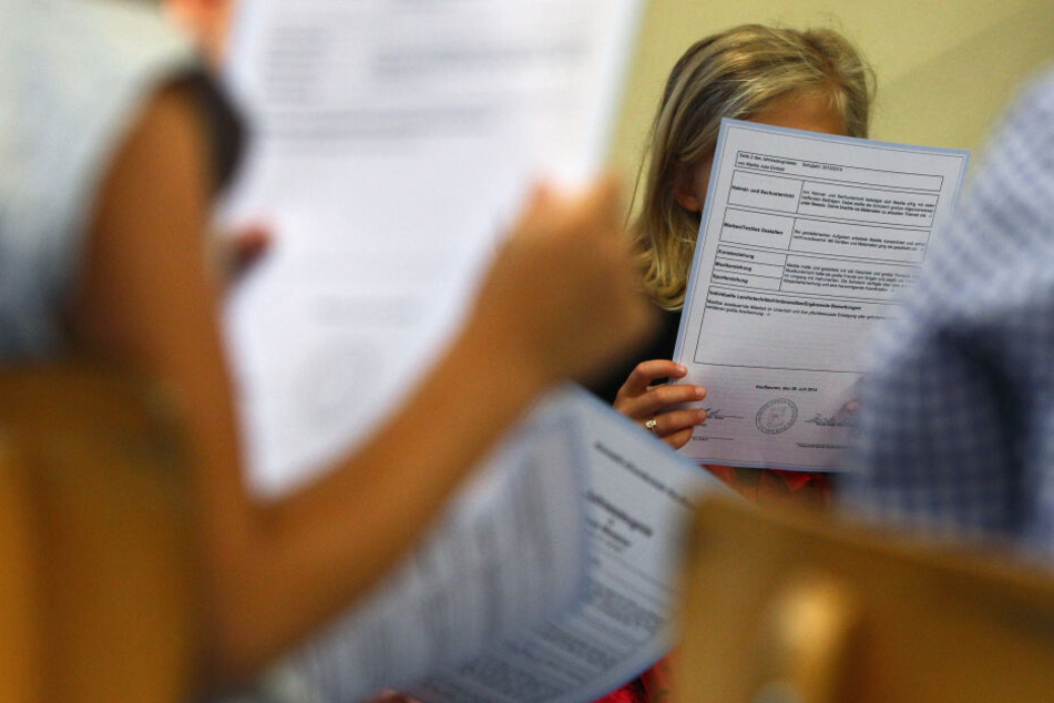 Schüler einer ersten Klasse sitzen in einer Grundschule und lesen ihre Zeugnisse.