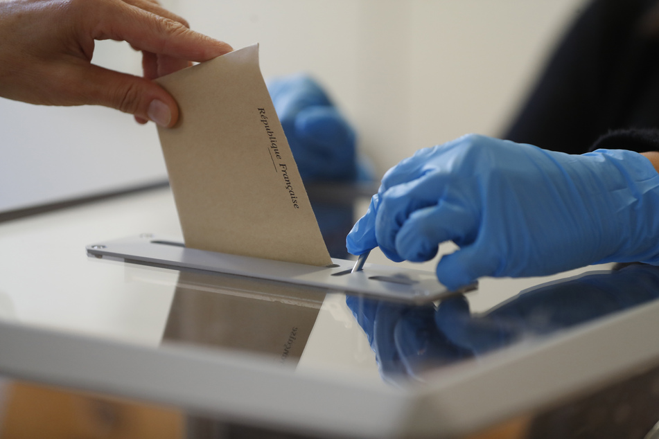 Ein Wahlhelfer mit Schutzhandschuhen öffnet die Wahlurne für eine Abstimmung während des ersten Wahldurchgangs der Kommunalwahlen.