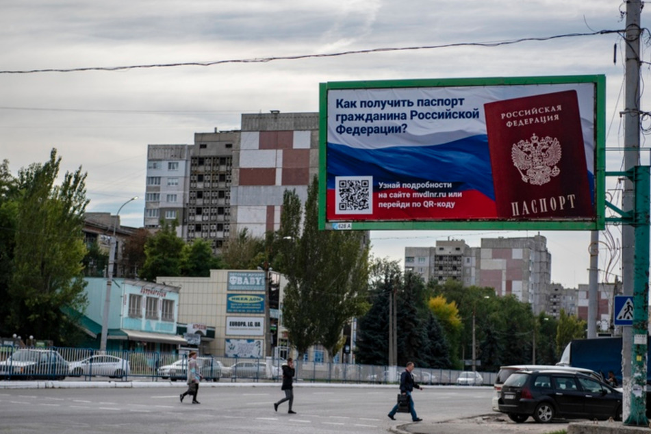 Menschen überqueren eine Straße mit einem Plakat mit der Aufschrift "Wie man den Pass eines russischen Bürgers bekommt" vor dem Scheinreferendum in der von den von Russland unterstützten Separatisten kontrollierten Volksrepublik Luhansk in der Ostukraine.