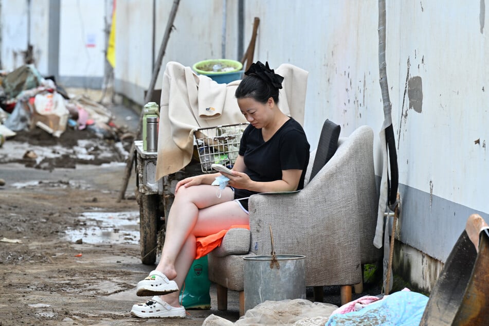 A resident seated on a couch checks her mobile phone while cleaning her house following deadly flooding in Taishitun village, Miyun district, Beijing on August 5, 2025.