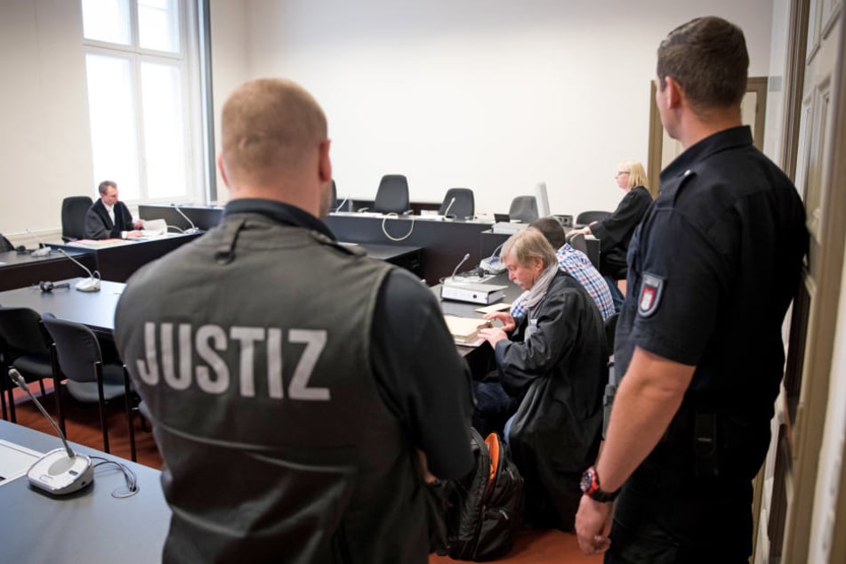 Rechtsanwalt Wilfried Behrendt (Mitte) und sein Mandant sitzen vor Prozessbeginn in einem Gerichtssaal im Strafjustizgebäude.
