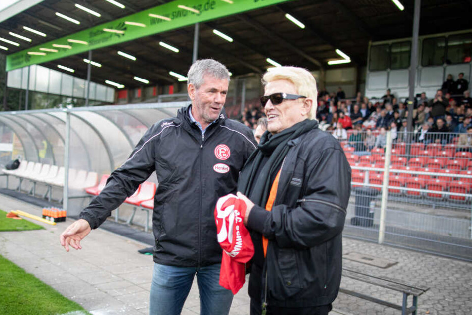 Heino (80) steht vor den Anstoß für das Benefizspiel auf dem Spielfeld neben Fortuna Trainer Friedhelm Funkel (65).