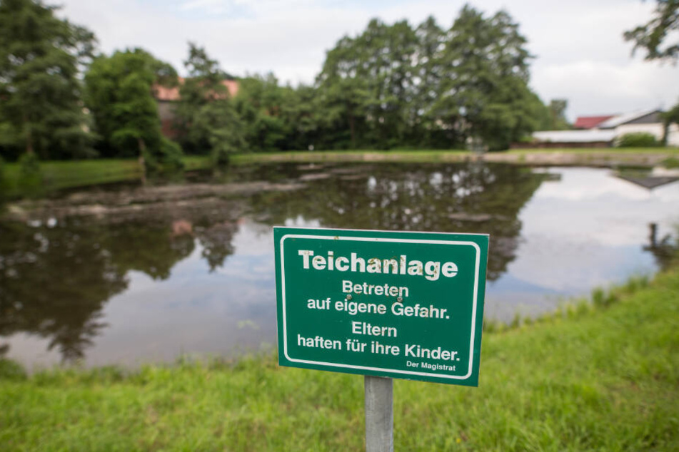 Ein Schild mit der Aufschrift "Teichanlage Betreten auf eigene Gefahr. Eltern haften für ihre Kinder." weist auf eine Teichanlage hin.
