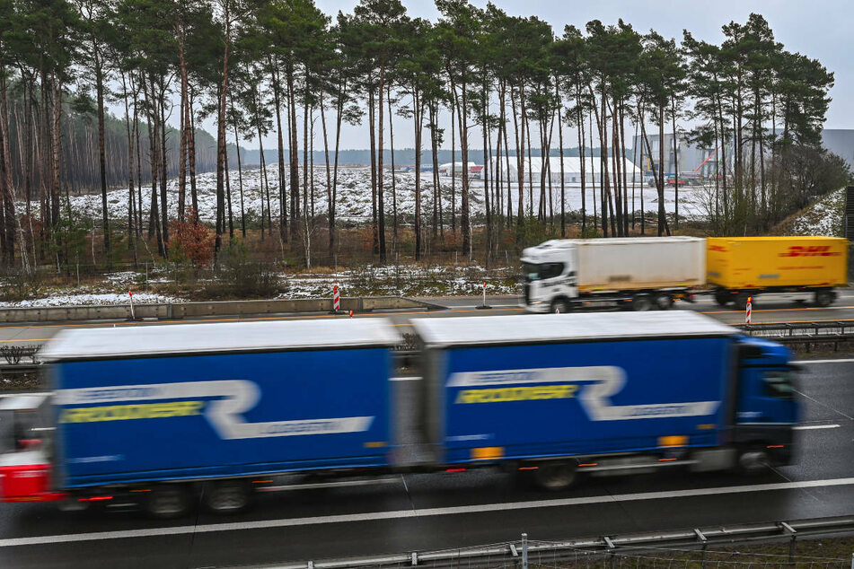 Lkw fahren auf dem östlichen Berliner Ring der Autobahn 10 am Baugelände der Tesla Gigafactory vorbei. Zwei Umweltverbände wollen den geplanten Bau der temporären Anschlussstelle an das Werk vorläufig stoppen.