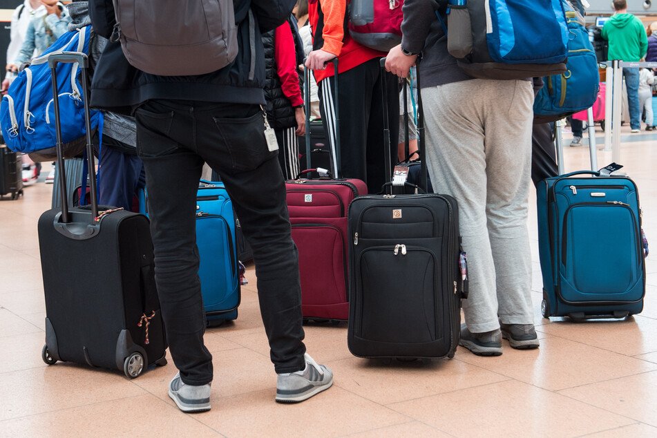 Reisende stehen mit ihrem Gepäck am Flughafen. Droht für Freitag auch in Hamburg ein Chaos?