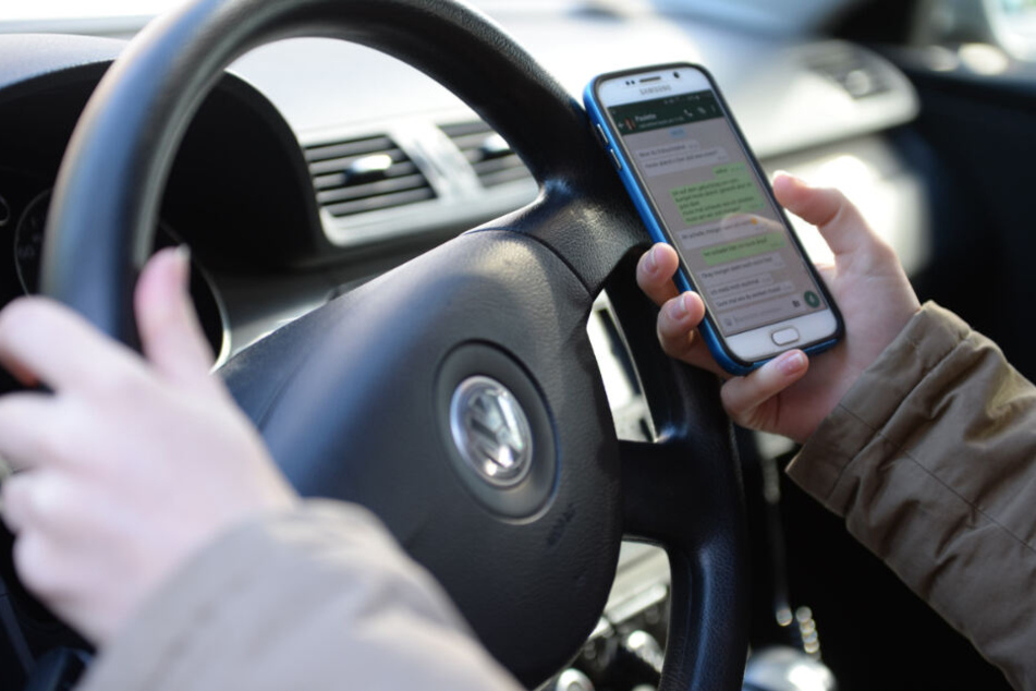 Eine Frau sitzt im Auto am Steuer und liest Nachrichten auf ihrem Smartphone.