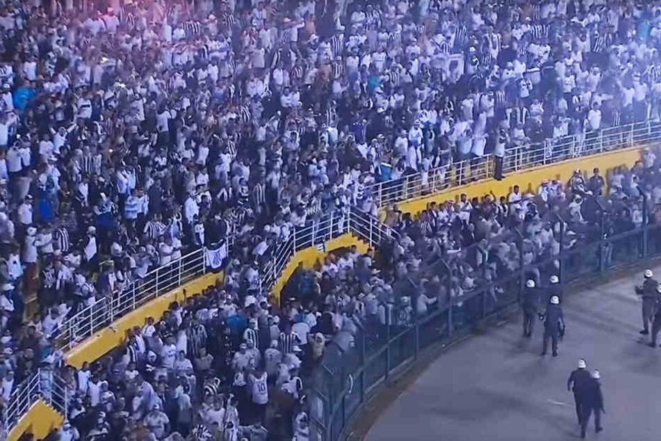 Die Santos-Anhänger haben die Balustrade überwunden. Nur ein wackliger Zaun und ein paar wenige Polizisten trennen sie noch vom Spielfeld.