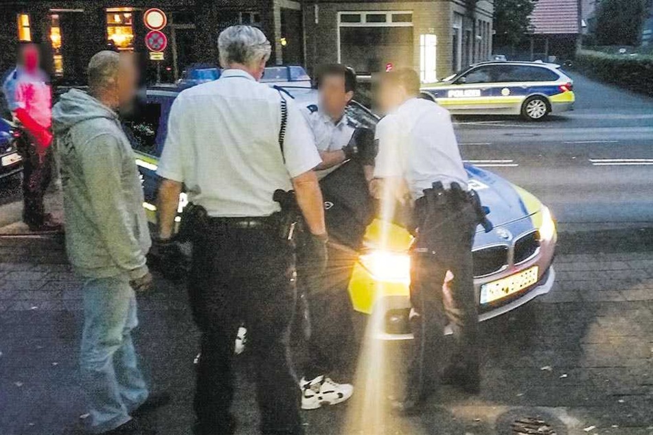 Polizisten fixieren den Mann auf der Motorhaube des Streifenwagens.