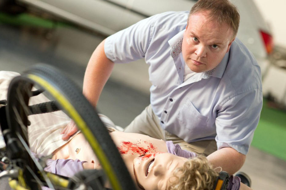 Eugen Latka stellt einen Fahrradunfall nach, dabei blutet und stöhnt die Puppe wie ein Mensch.