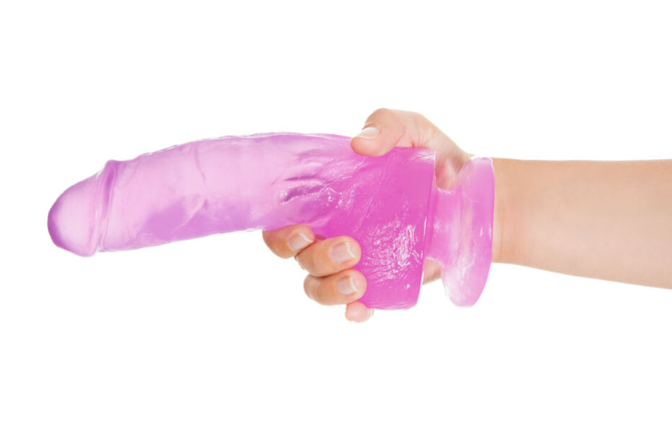 Eine Hand hält einen durchsichtigen Dildo. (Symbolbild)