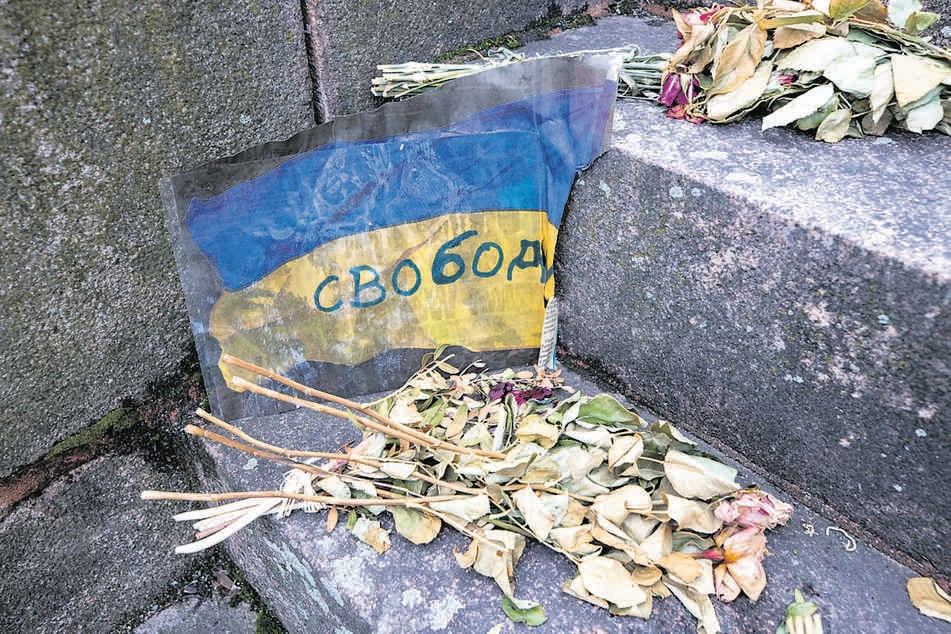 Das Bild einer ukrainischen Fahne wurde samt Blumen an dem Denkmal abgelegt.