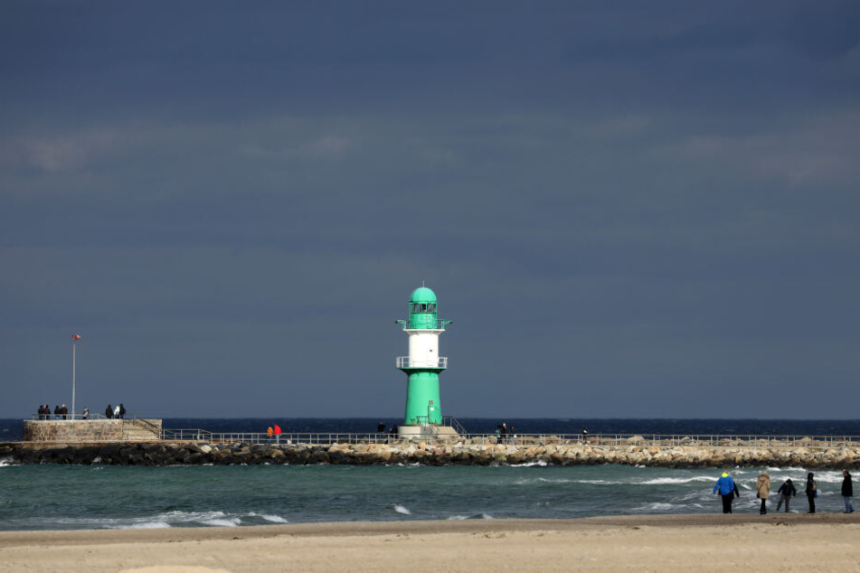 Ein kurzer sonniger Abschnitt hellt den Ostseestrand und den Leuchtturm auf, während dunkle Wolken des Sturmtiefs "Bennet" über die Ostsee in Mecklenburg-Vorpommern ziehen.