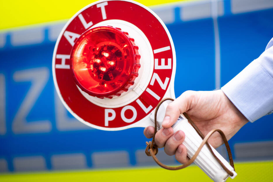 Ein Polizist hält während eines Presstermins eine Polizeikelle mit der Aufschrift "Halt Polizei" in der Hand.