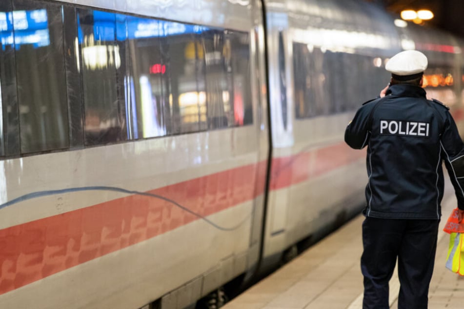 Ein ICE steht im Hauptbahnhof einer deutschen Großstadt, während daneben ein Polizeibeamter telefoniert.