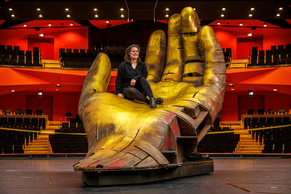 Bühnenbildnerin Anna Schöttl (35) sitzt in der goldenen Riesenhand. Sie kann über die Bühne gefahren werden und ein Finger ist beweglich.