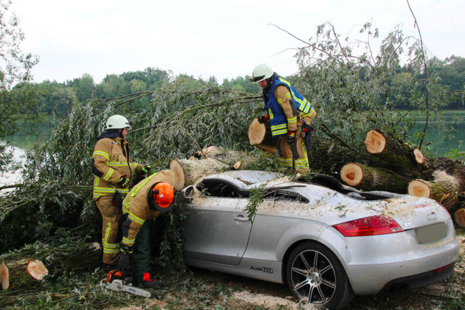 Feuerwehrleute zersägen einen Baumstamm, der am Roither See auf ein Auto gefallen ist.