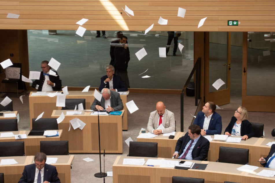 Die Abgeordneten sitzen im Landtag, während Flugblätter auf sie rieseln.
