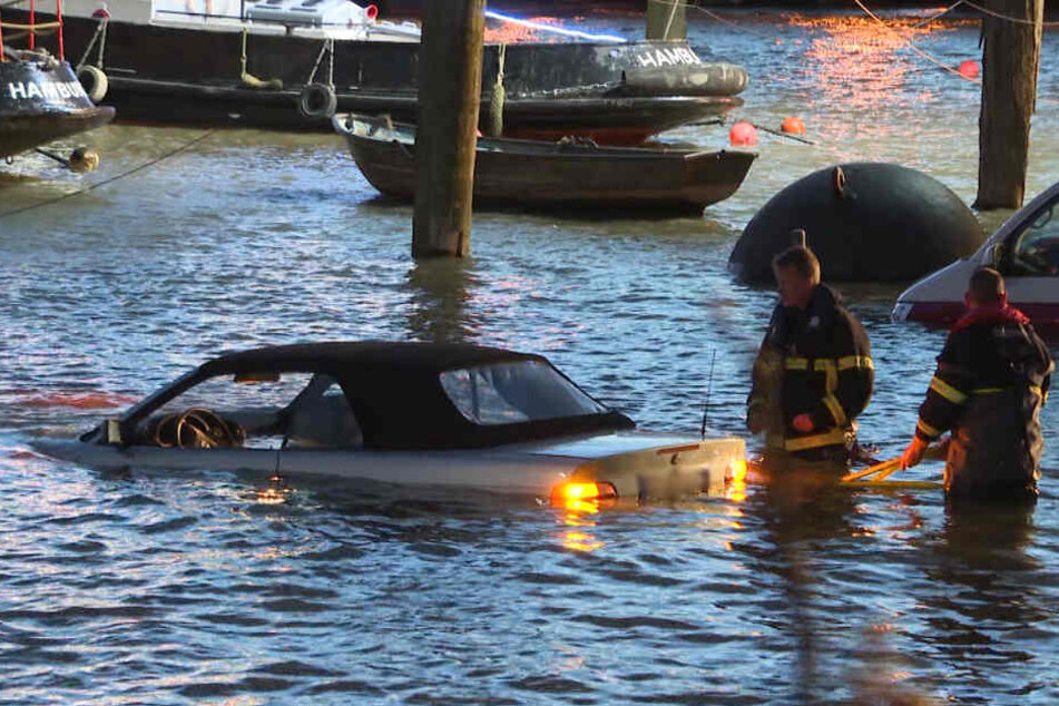 Die Einsatzkräfte stehen hüfttief vor einem geparkten Auto im Wasser.