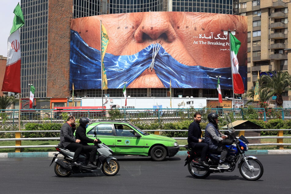 Motorists make their way past an billboard referring to President Donald Trump and the Strait of Hormuz, installed on a building at the Valiasr Square in Tehran on May 2, 2026.